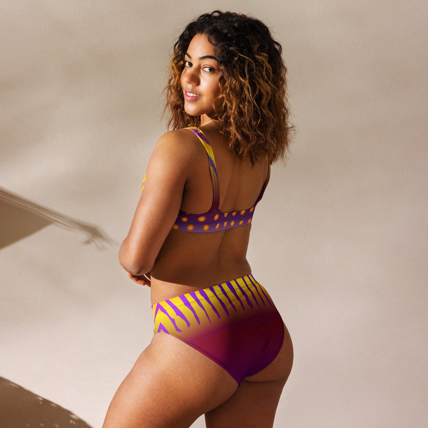 Woman Modeling the Betta Sawng Bikini Swimsuit in purples, oranges, yellows, and green patterns from the back looking over her shoulder.