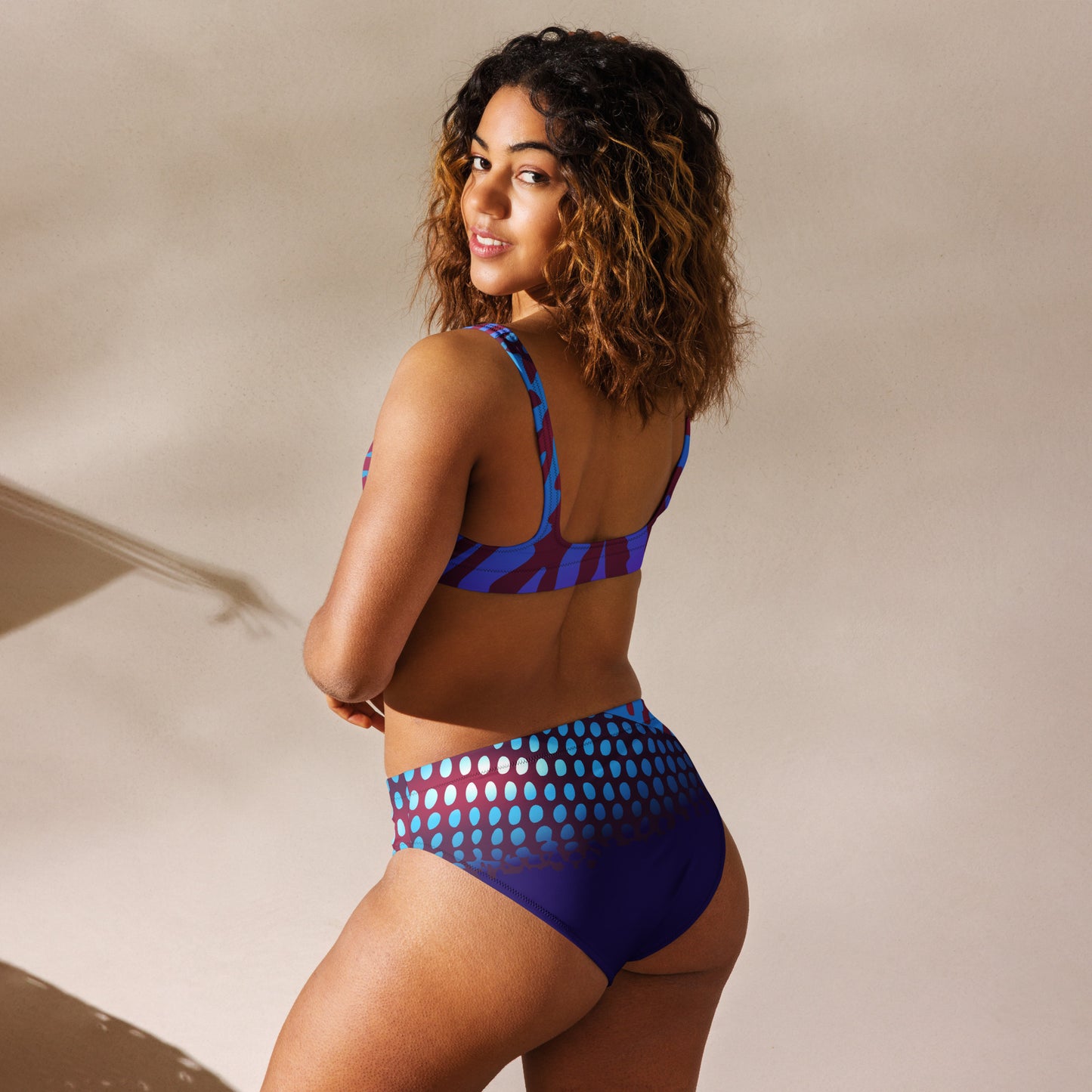 Woman modeling the Betta Ruk Bakini Swimsuit in purples, reds, and blue patterns from the left back.