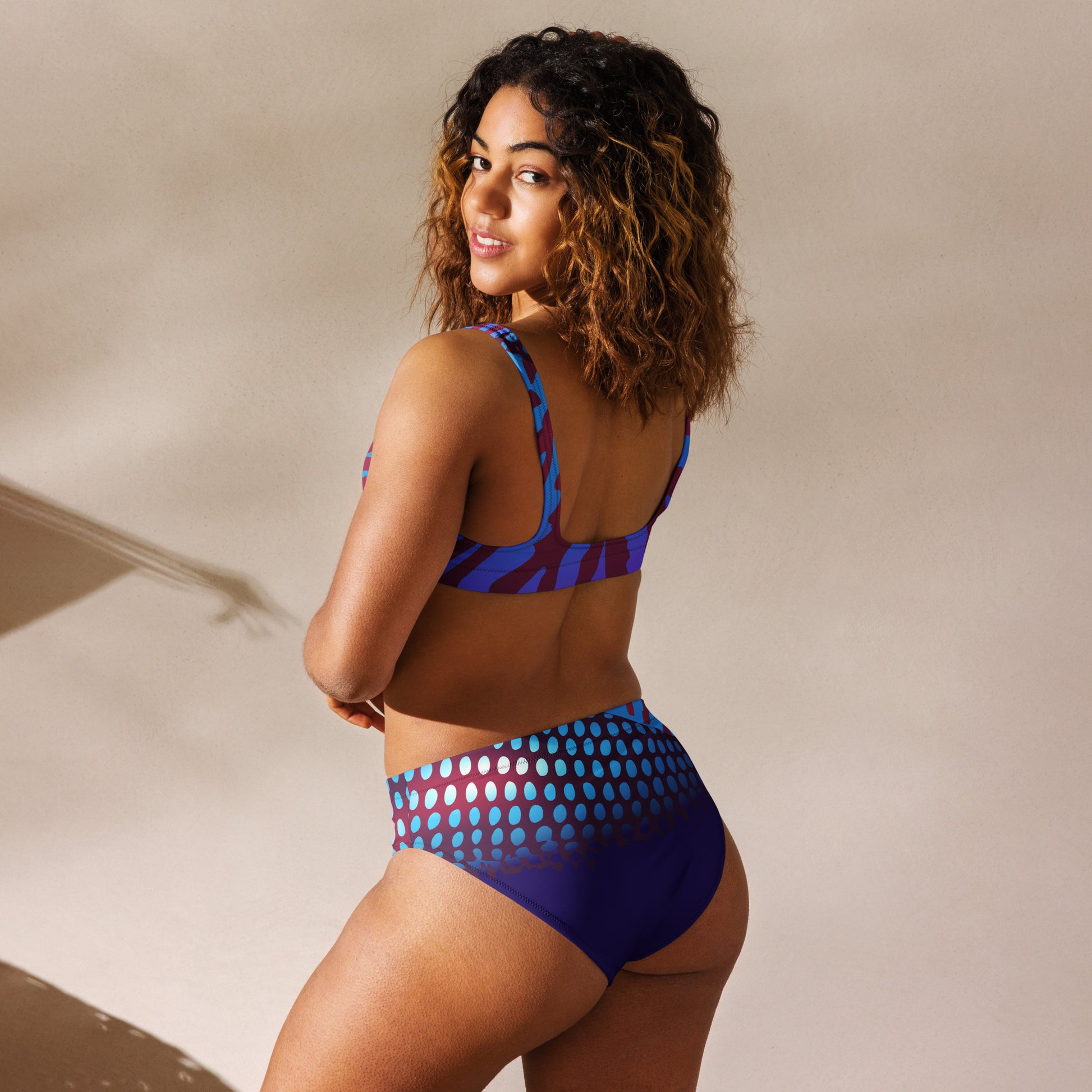Woman modeling the Betta Ruk Bakini Swimsuit in purples, reds, and blue patterns from the left back.
