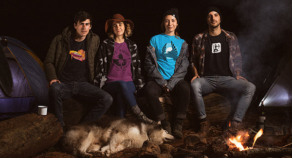 Four people sitting by a campfire wearing House Ullr Designed T-shirts.